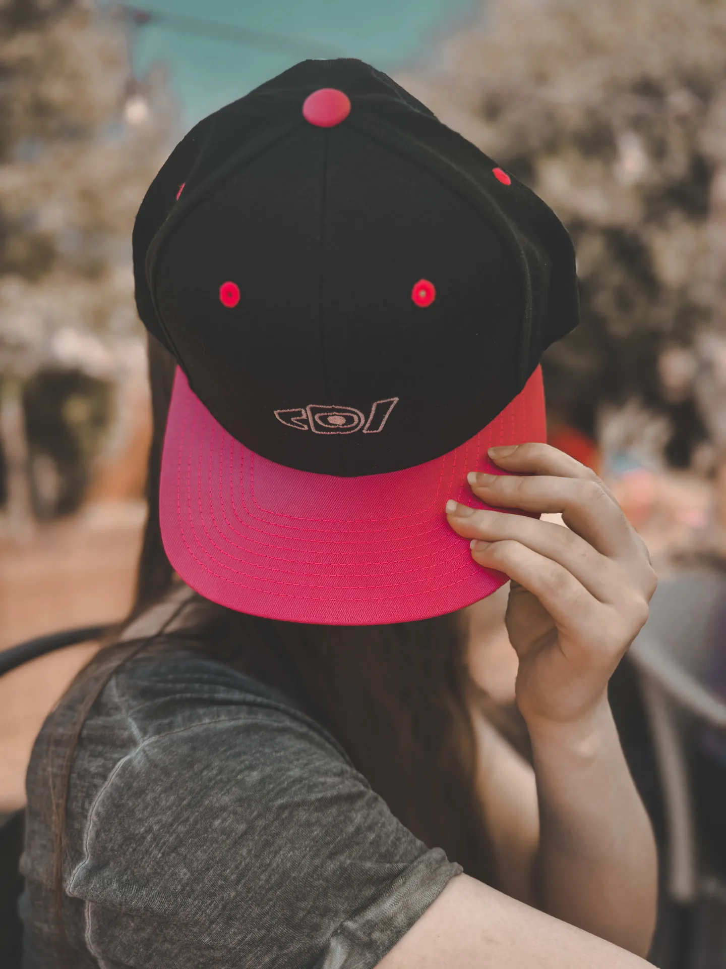 Model holding a black and neon pink Deafiant rose snapback in front of their face.