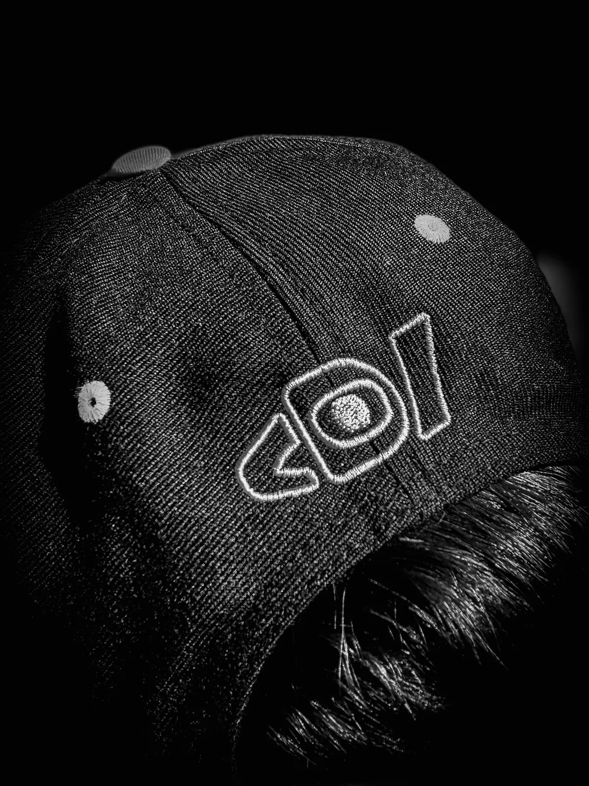 Black-and-white close-up of the Deafiant eye logo stitched on a black cap.