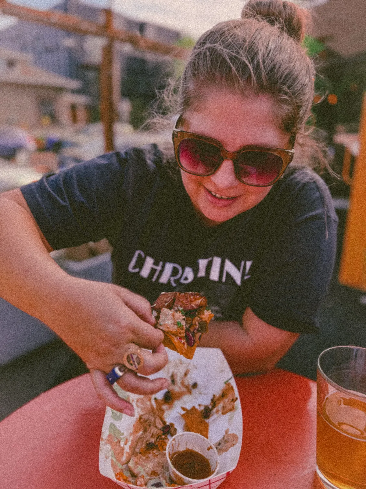 Model in a dark tee eating pizza at a red patio table.