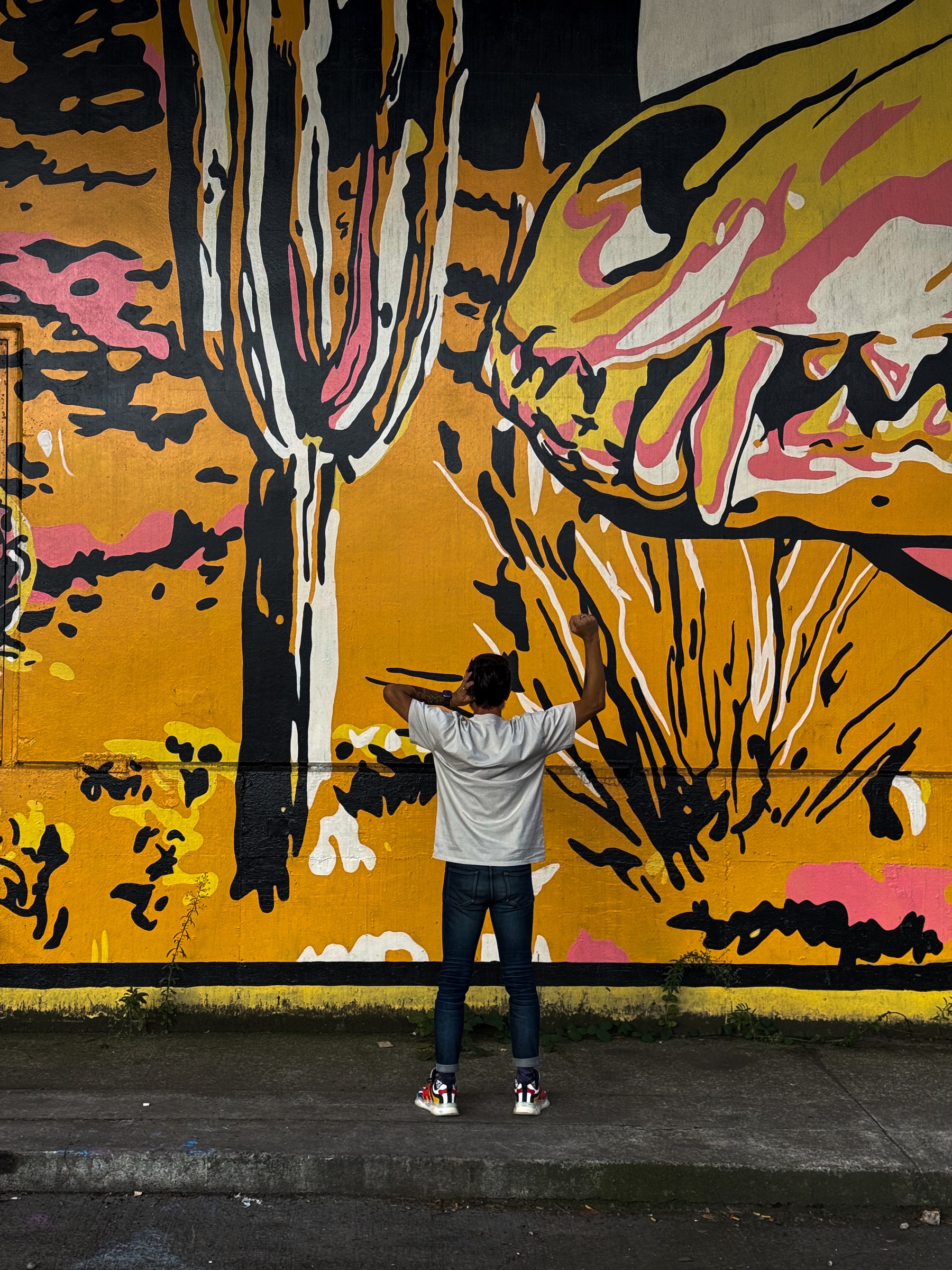 Man signing DEAF POWER, facing a large yellow and black mural of a cactus and skull along the Avenue of Murals on Hawthorne in Portland, OR