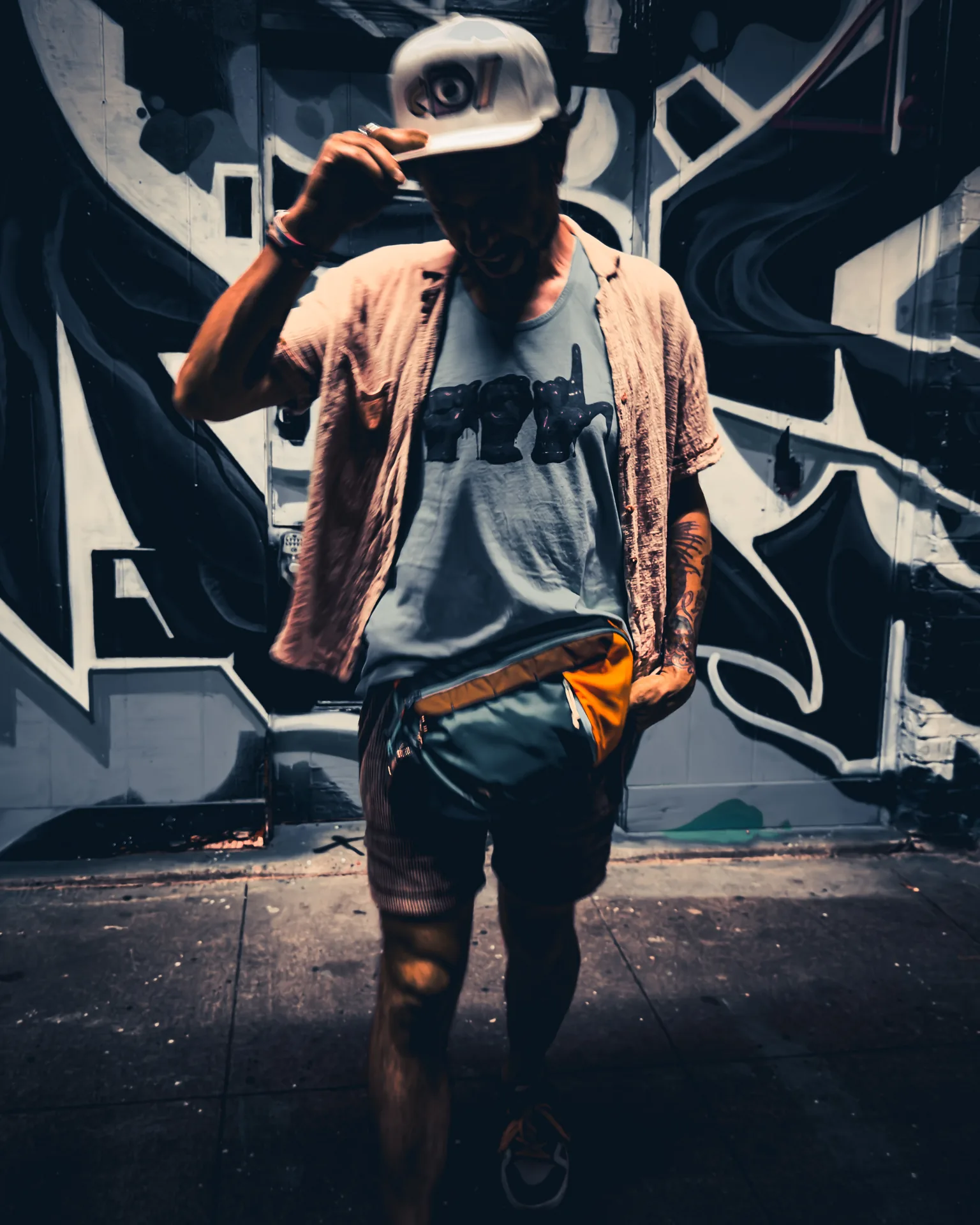 Model in a white Deafiant snapback walking past graffiti murals at night
